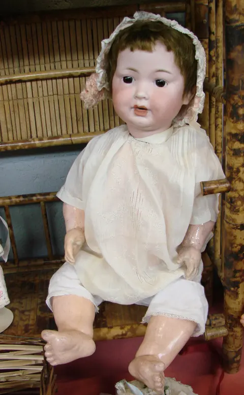 An antique bisque-head character baby doll wearing a lace bonnet and christening gown
