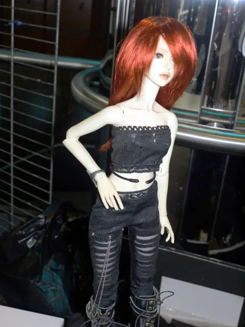 A modern resin ball-jointed doll with red hair and a black outfit, showing visible joint articulation