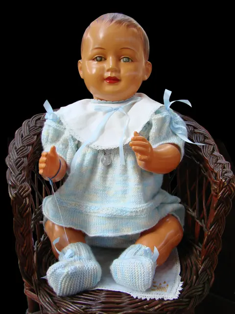 An antique celluloid baby doll with painted hair, dressed in a white lace bonnet-collar outfit