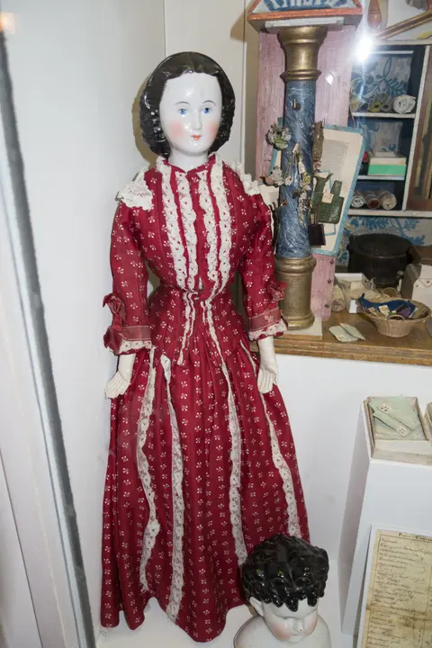 An antique porcelain-head doll with glossy molded black hair, wearing a red patterned Victorian dress