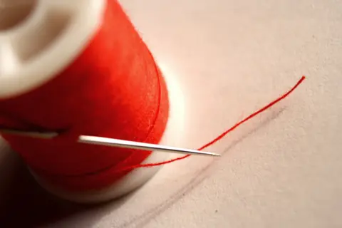 A needle threaded with red cotton thread, close up