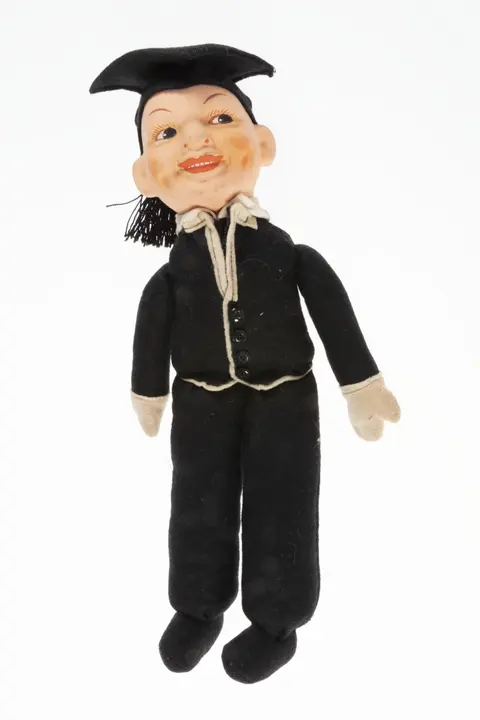 A 1920s-1930s American composition doll dressed in black graduation clothes and a mortarboard hat