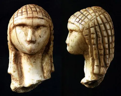 Front and side views of a small carved ivory head with a checkerboard-patterned hairstyle