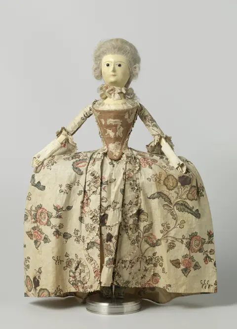 An 18th-century wooden fashion doll with glass eyes and a human-hair wig, dressed in a floral gown