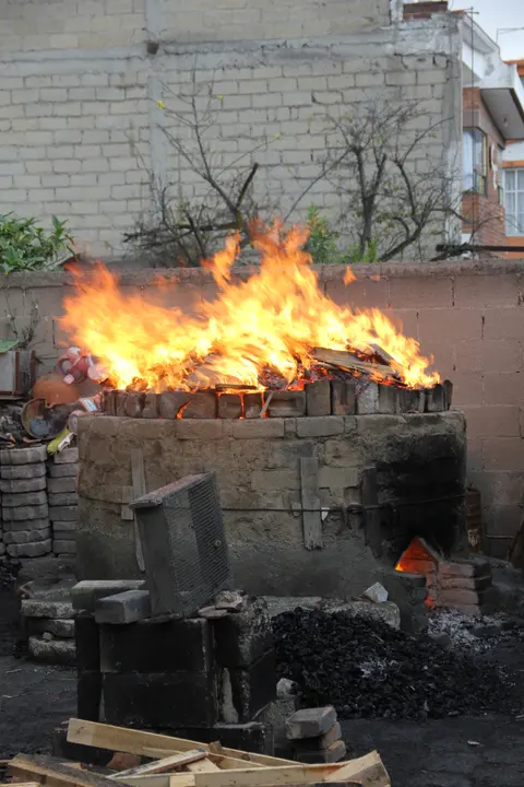 A traditional kiln firing at high temperature, flames visible at the mouth