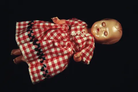 A small pink hard-plastic baby doll with painted sleeping eyes, in a red-and-white checked dress