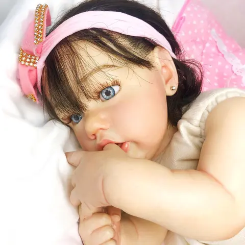 Close-up of a hyper-realistic reborn baby doll with rooted hair and glass eyes, sucking its own finger