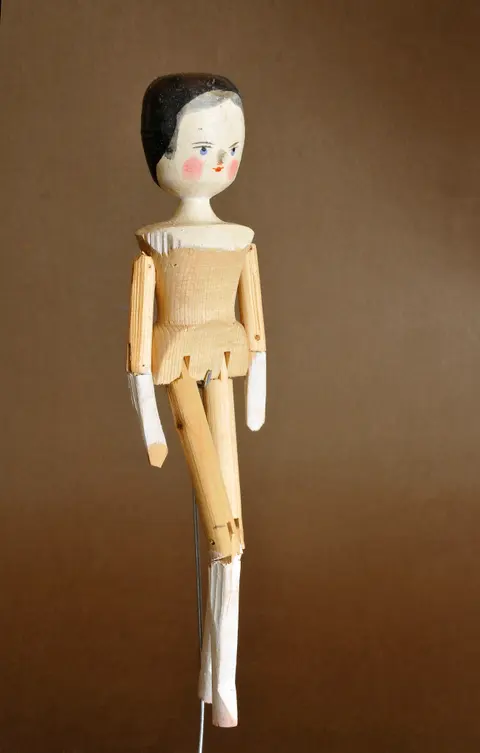 An unclothed wooden peg-jointed doll with a painted face, standing against a plain background